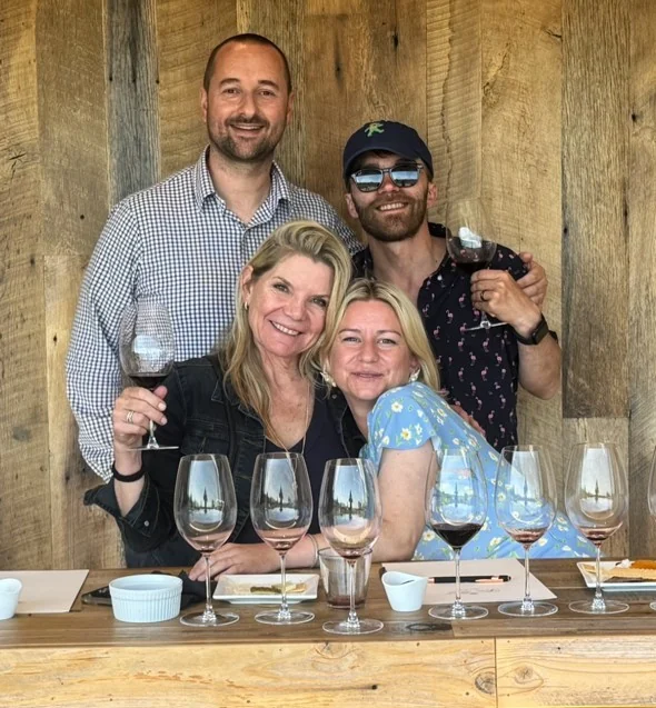 Vince and three guests behind wine glasses at a tasting room.