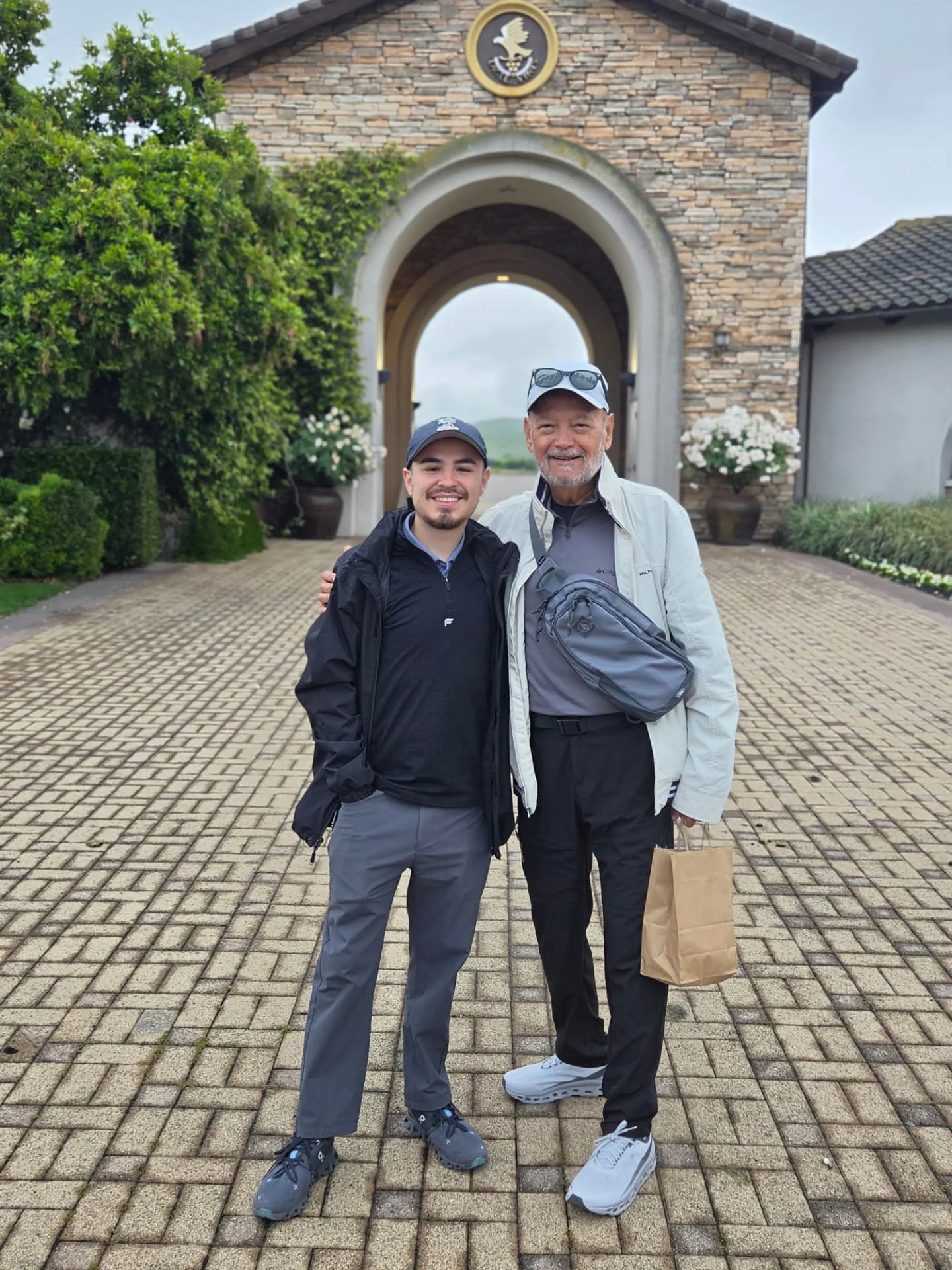 Two men at a stone winery entrance beneath an arch.