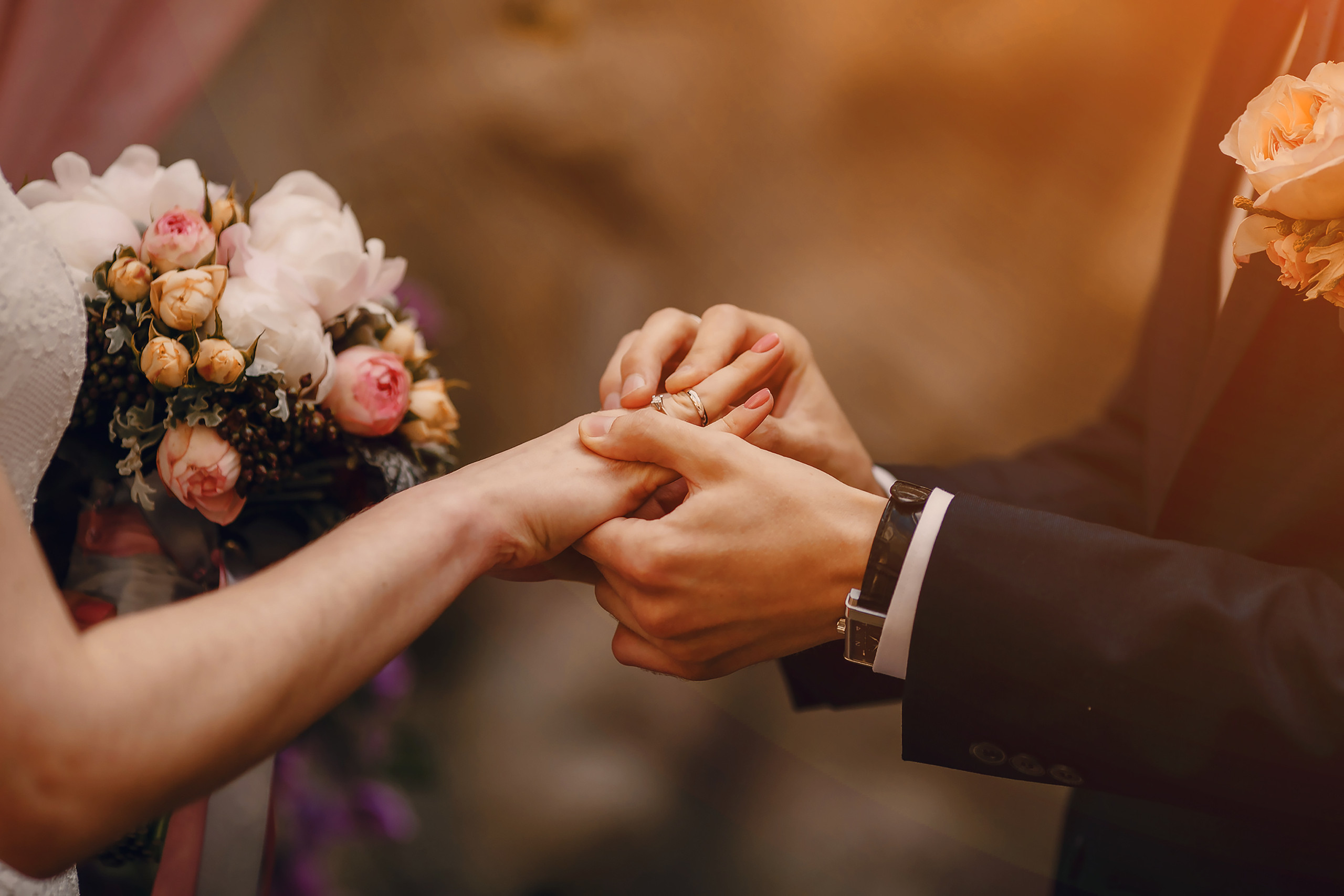 Intimate wedding ceremony moment with hands exchanging rings and a beautiful bridal bouquet of white and pink roses