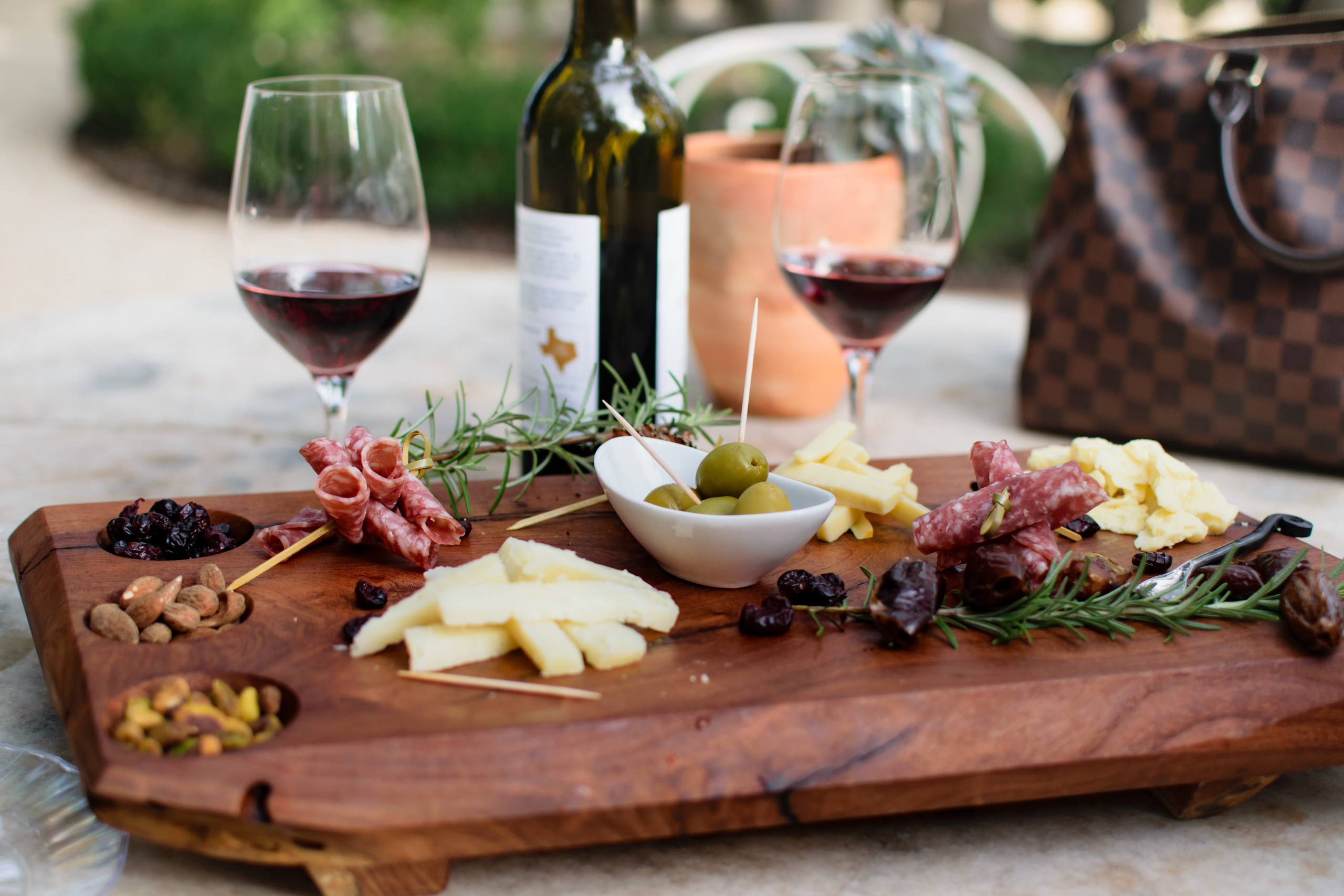 Elegant wine tasting setup with two glasses of red wine, charcuterie board, cheeses, and fresh rosemary on a wooden table in a Napa Valley winery